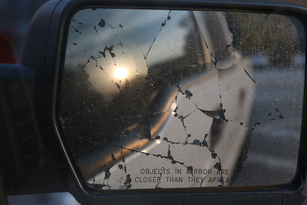 A broken side mirror on a work truck reflecting the rising sun.