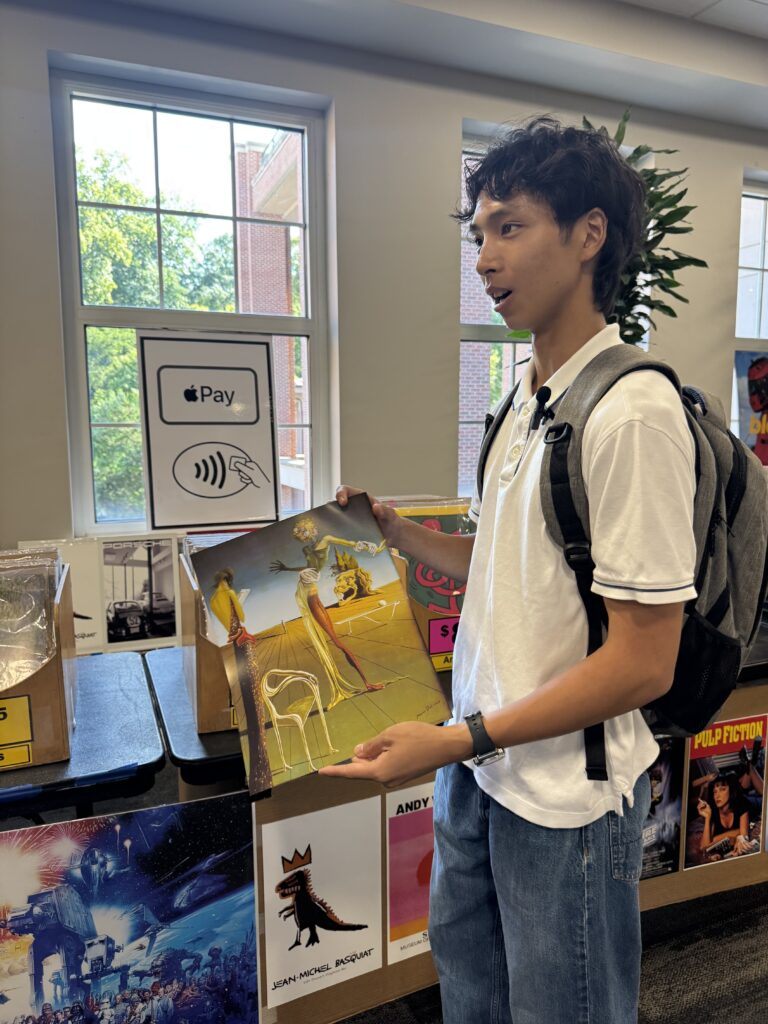 A college student stands holding a poster in a campus building