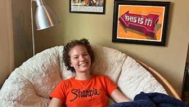 Sydney sits in a circular chair in front of her print collection.