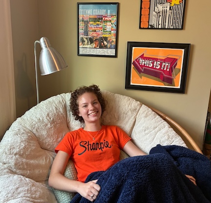 Sydney sits in a circular chair in front of her print collection. 
