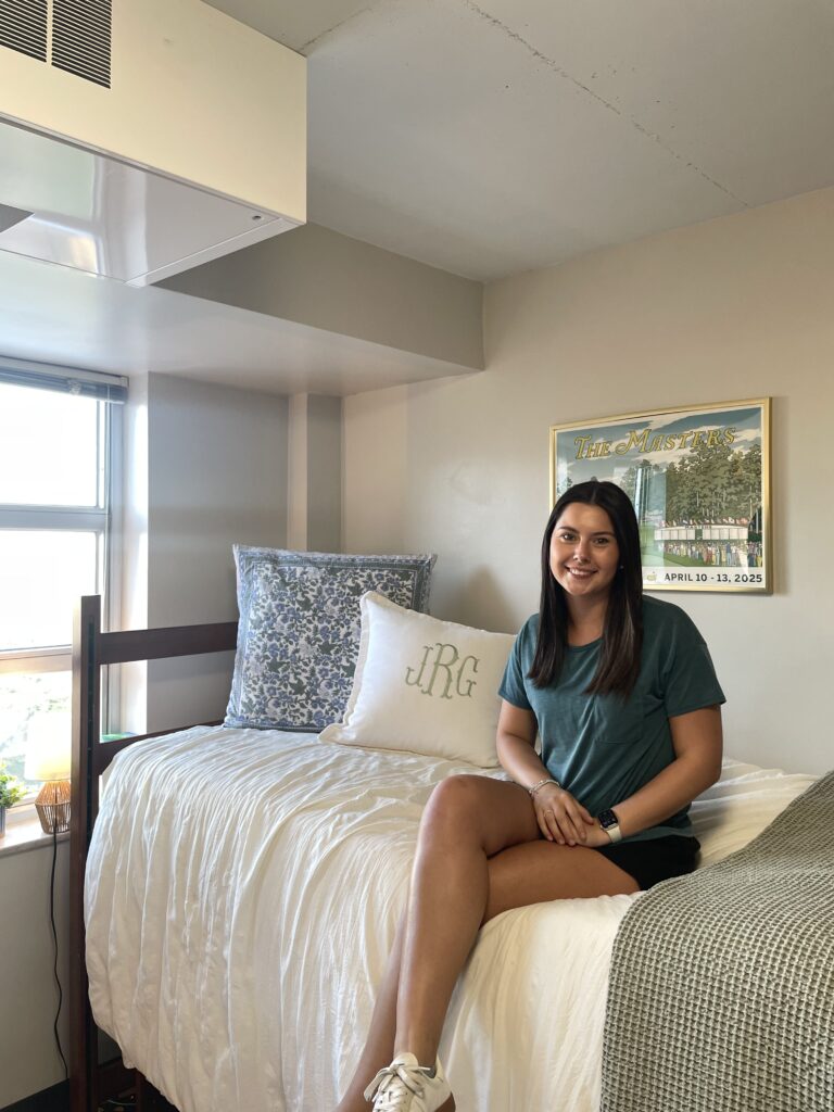 Julia Randall sits on her lofted bed in her room in Brumby Hall. Randall's room is decorated with cream and blue tones and keeps her blinds open.