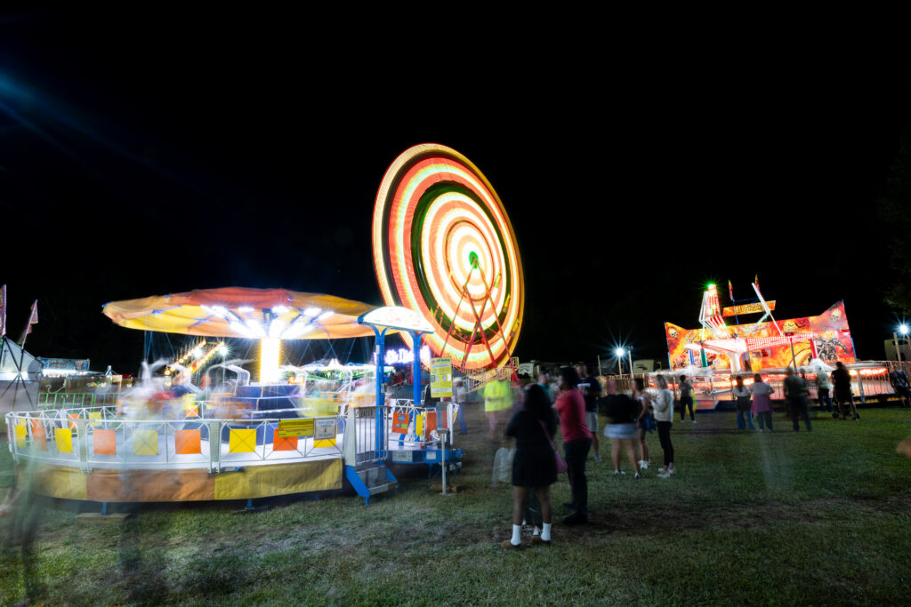 spinning lights shine above people walking at the fair