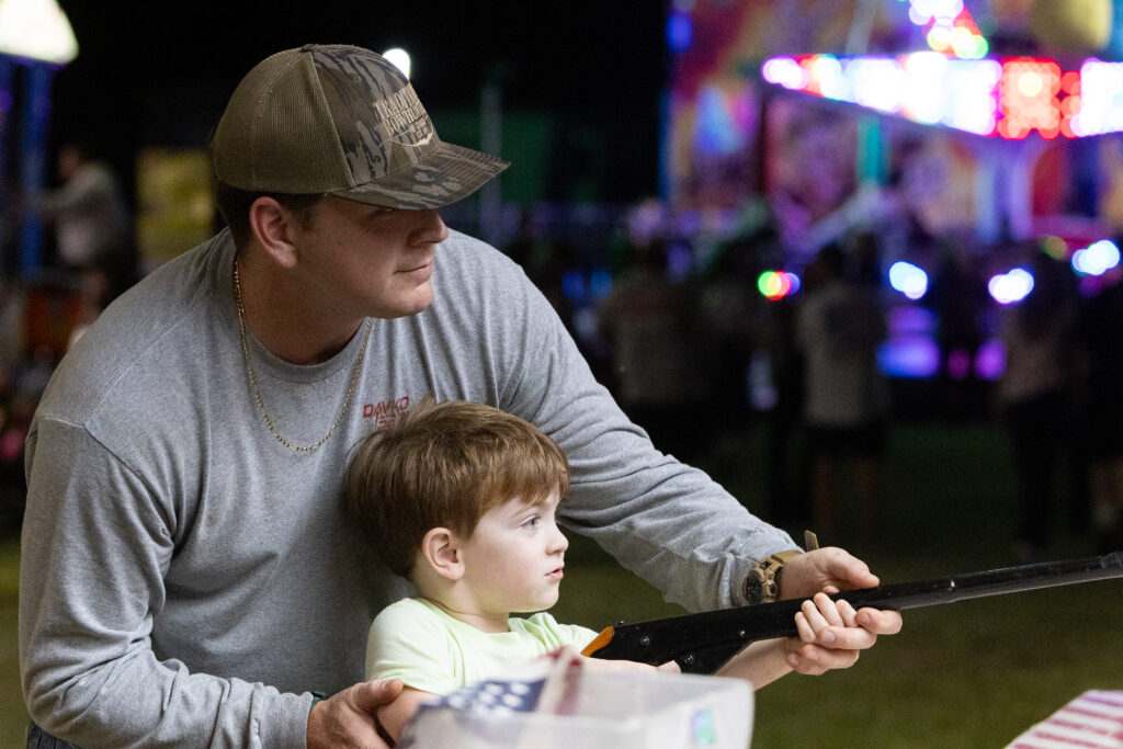 a man and a boy play a shooting game at a fair