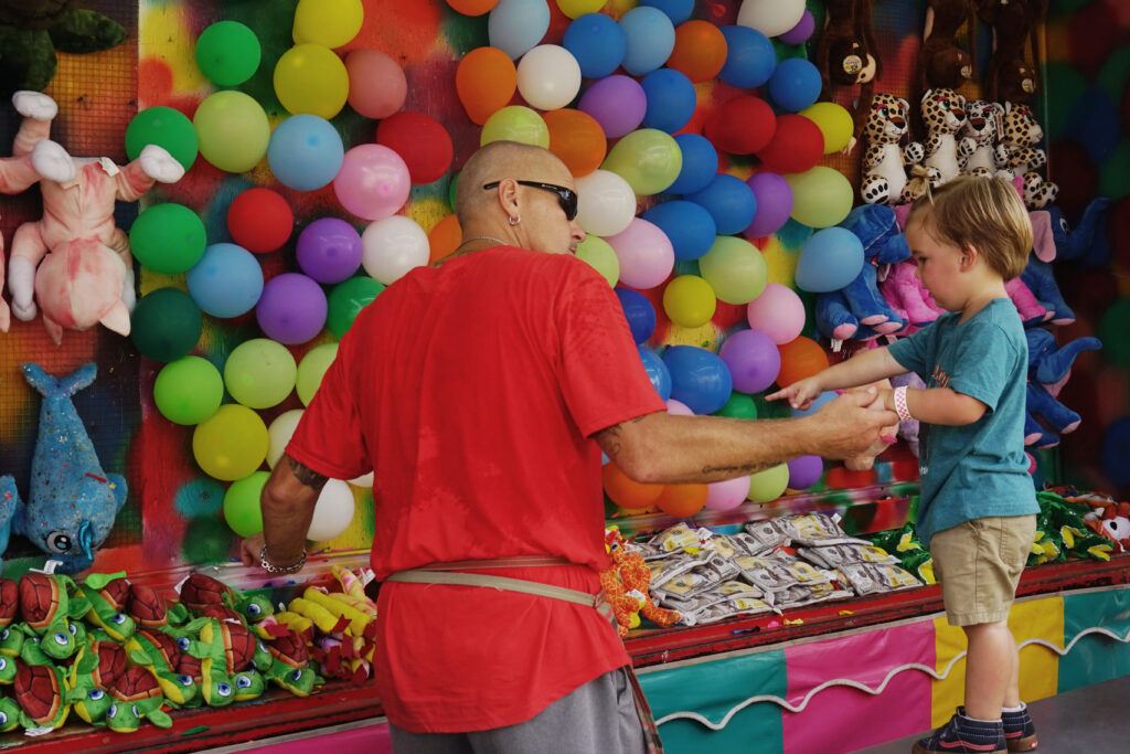 A man running a fair game helps a child play