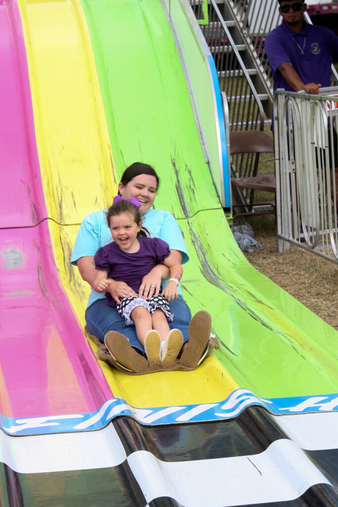 Two people sitting together go down a yellow slide at the fair