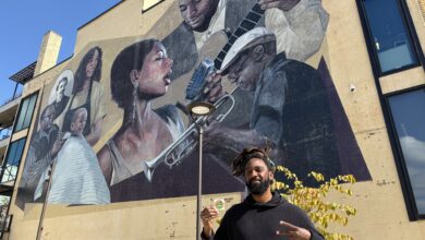 Man stands and holds voting sticker in front of mural on building