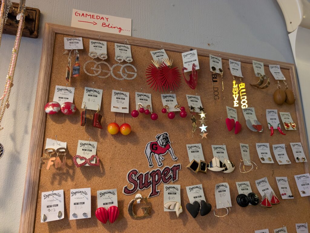 Earrings are displayed on a corkboard underneath a sign promoting "gameday bling" inside of Dynamite Clothing in Athens, Georgia.