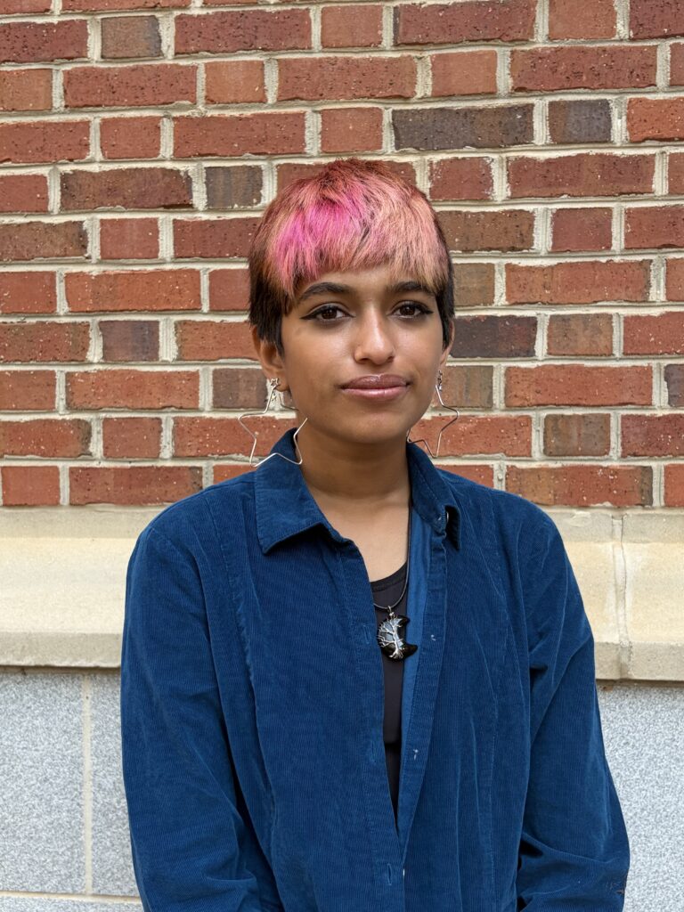 Maya Shrivastav poses for a photo in front of a brick building.